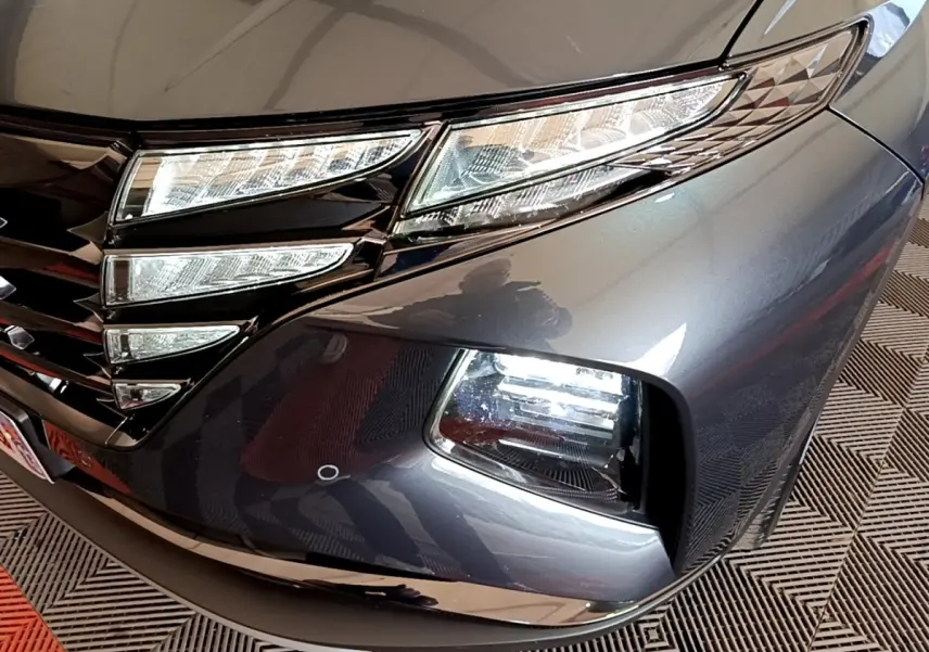 Gros plan sur l'avant droit gris foncé du Hyundai Tucson 2022, mettant en valeur les phares LED et la calandre noire brillante.