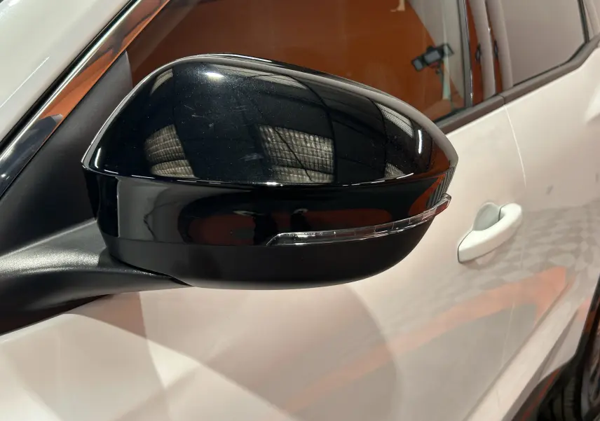 Gros plan sur le rétroviseur noir brillant côté gauche d’un Renault Austral blanc nacré, avec poignée de porte visible.