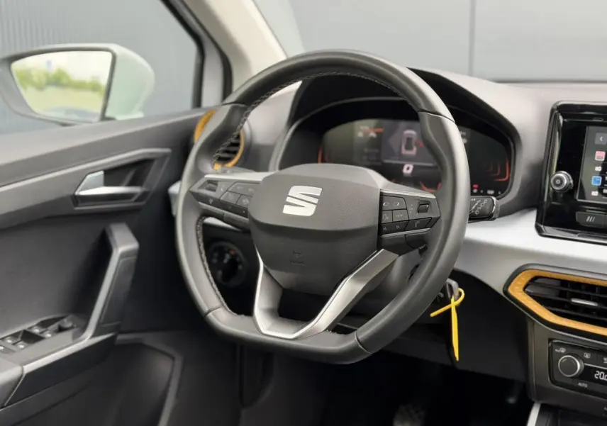 Vue intérieure côté conducteur du volant et tableau de bord du SEAT Arona TSI 115 Style avec inserts jaunes et écran tactile.