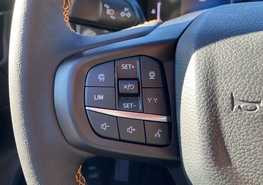 Gros plan sur les commandes au volant du Ford Ranger 2.0 205 Wildtrak Plus 2025, cuir noir avec surpiqûres orange.