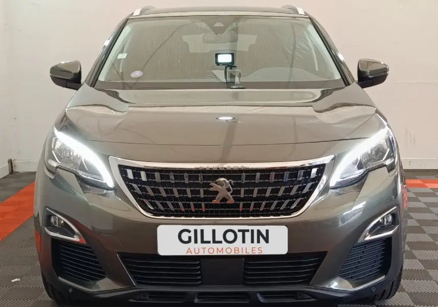 Vue frontale d'un Peugeot 3008 gris foncé avec phares LED allumés et calandre chromée distinctive.