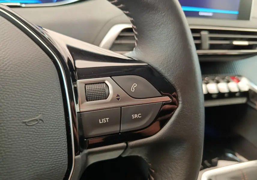 Gros plan sur les commandes gauche du volant cuir du Peugeot 3008 gris foncé, avec tableau de bord en arrière-plan.