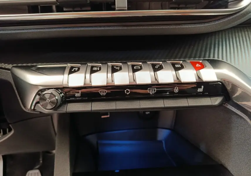 Gros plan sur la rangée de boutons argentés et noirs du tableau de bord du Peugeot 3008 gris foncé, avec commandes climatisation et hazard.