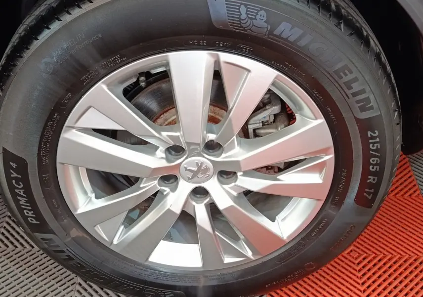 Gros plan sur la jante argentée avec logo Peugeot d'un 3008 gris foncé, pneu Michelin visible sur tapis rouge.
