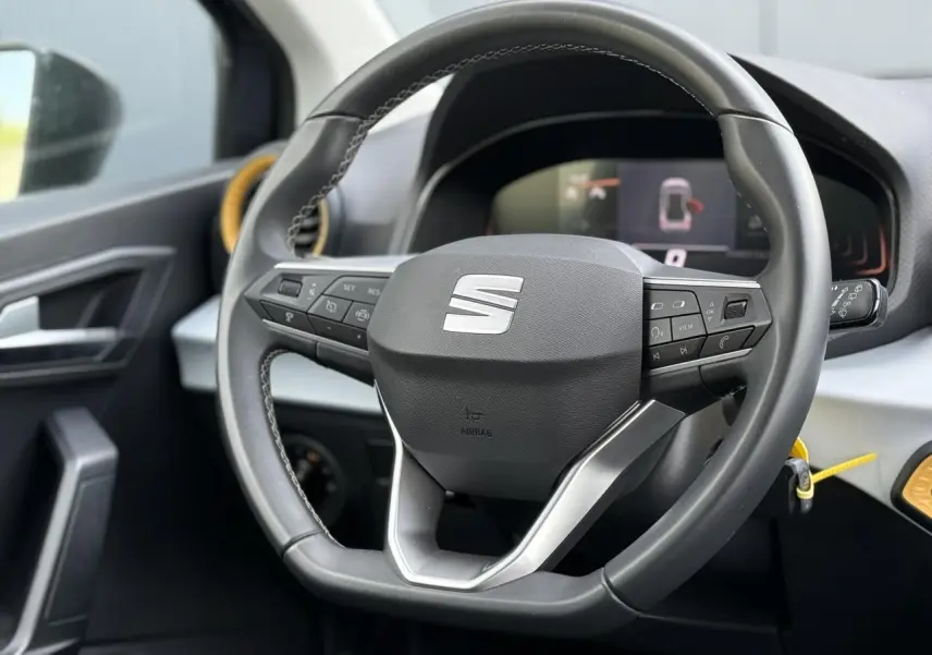 Vue rapprochée du volant multifonction noir de la SEAT Arona 2025 avec tableau de bord digital en arrière-plan.