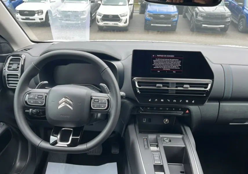 Vue intérieure avant du Citroën C5 Aircross blanc, volant cuir multifonctions et écran tactile central allumé.