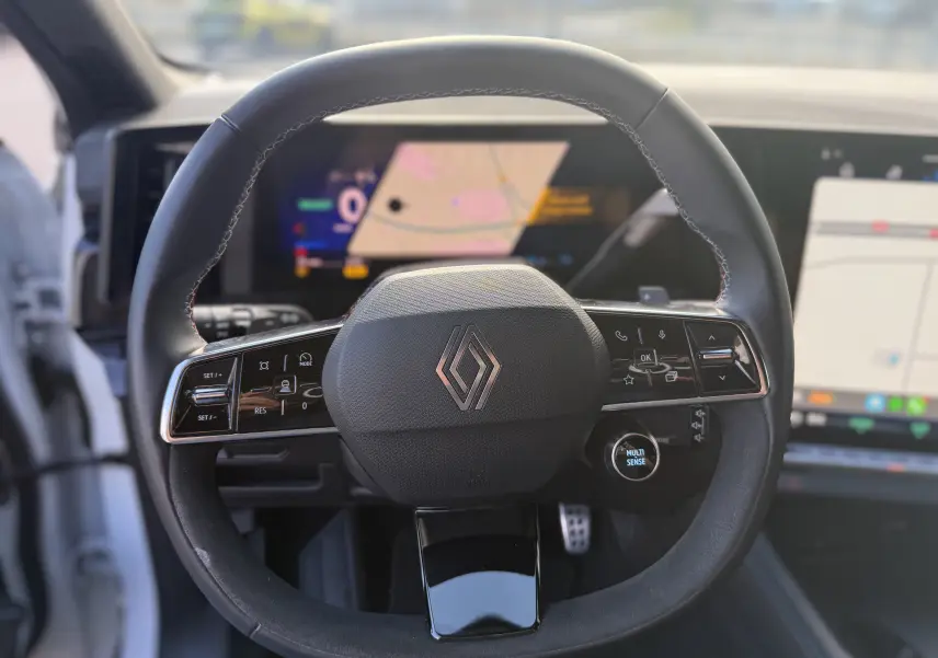 Vue centrée sur le volant noir du Renault Austral Hybrid 2025, avec commandes intégrées et écran numérique en arrière-plan.
