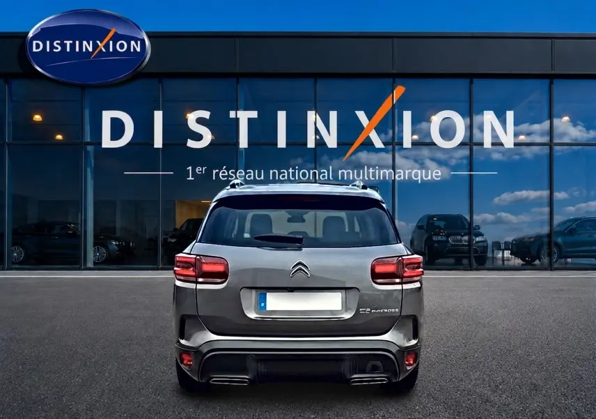 Vue arrière d'un Citroën C5 Aircross gris 2025 avec barres de toit et feux arrière LED, devant une vitrine Distinxion.