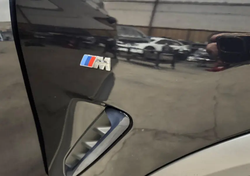 Gros plan sur l'aile avant gauche noire d'une BMW X4 M SPORT avec logo M coloré et prise d'air latérale.