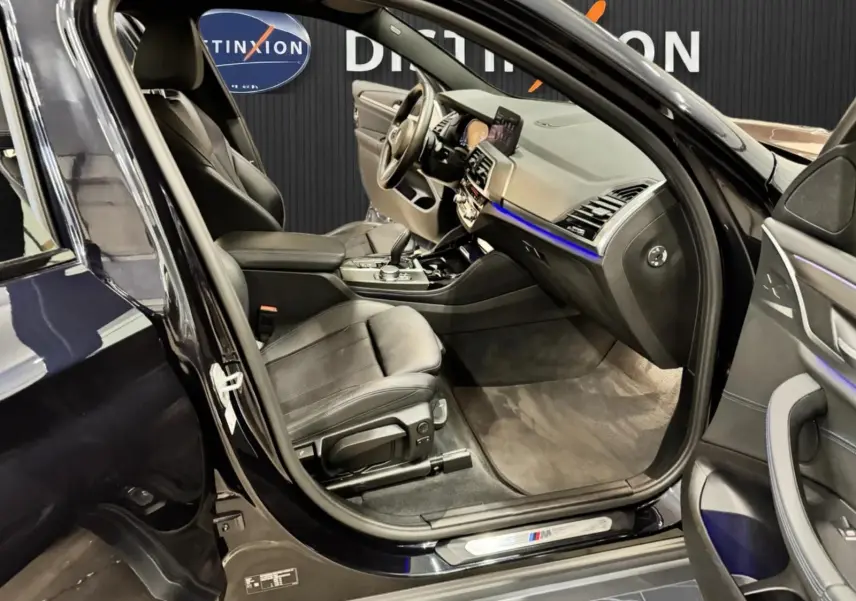 Vue intérieure côté conducteur de la BMW X4 XDrive 20d 2020 en Carbonschwarz, avec sièges cuir noir et éclairage d'ambiance bleu.