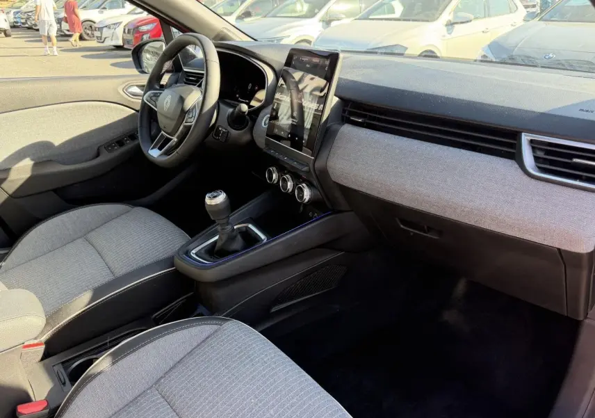 Intérieur avant droit de Renault Clio 2025, volant multifonction, sellerie grise, écran tactile vertical et boîte manuelle.