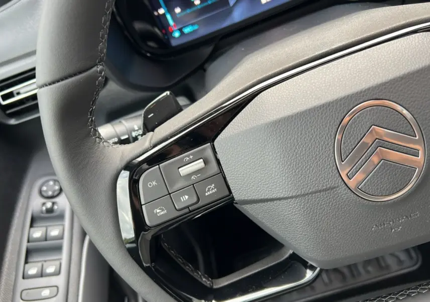 Gros plan sur le volant cuir du Citroën Berlingo 2025 avec commandes intégrées et logo chrome au centre.