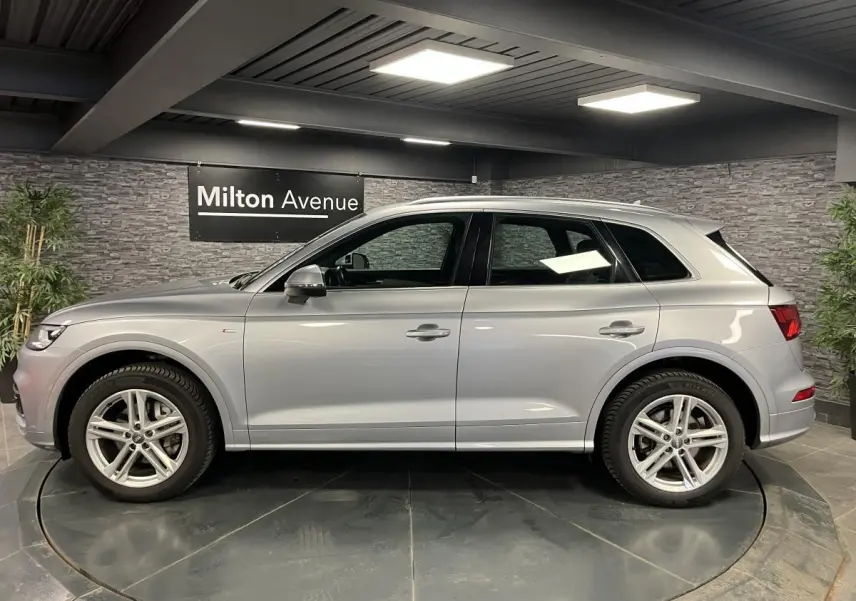 Profil côté gauche d'un Audi Q5 gris métallisé S line 2019 dans un showroom avec jantes 5 branches doubles.