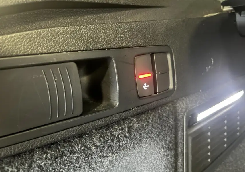 Gros plan sur le bouton de rabattement électrique des sièges dans le coffre d'un Audi Q5 gris S line 2019.