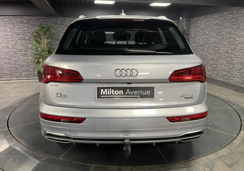 Vue arrière d'un Audi Q5 gris avec hayon électrique et crochet d'attelage rétractable visible en intérieur showroom.