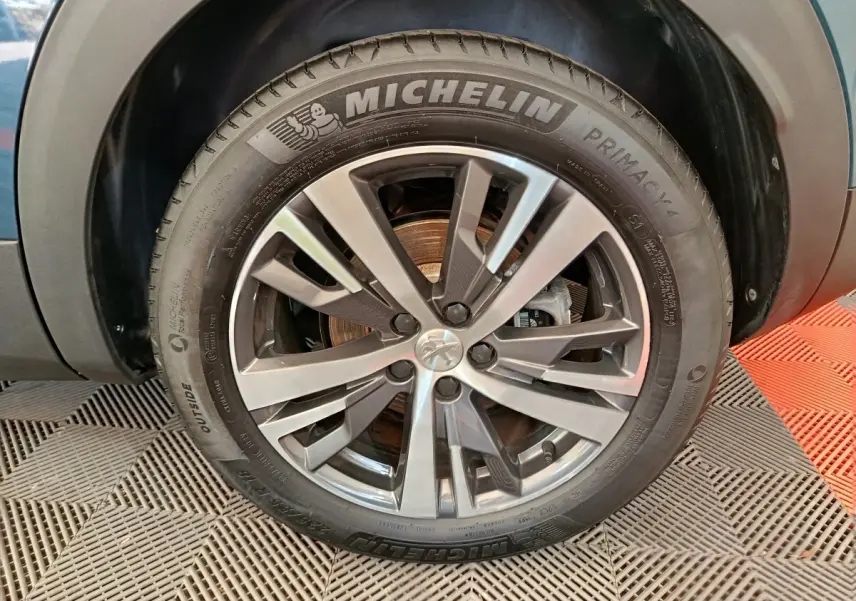 Gros plan sur la jante alliage et pneu Michelin d'un Peugeot 3008 bleu, mettant en valeur le design moderne.