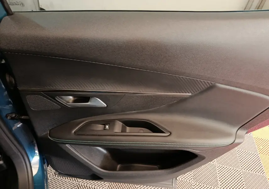 Gros plan sur la porte côté gauche du Peugeot 3008 bleu 2022, montrant la poignée, les commandes de fenêtre et la finition cuir avec surpiqûres vertes.