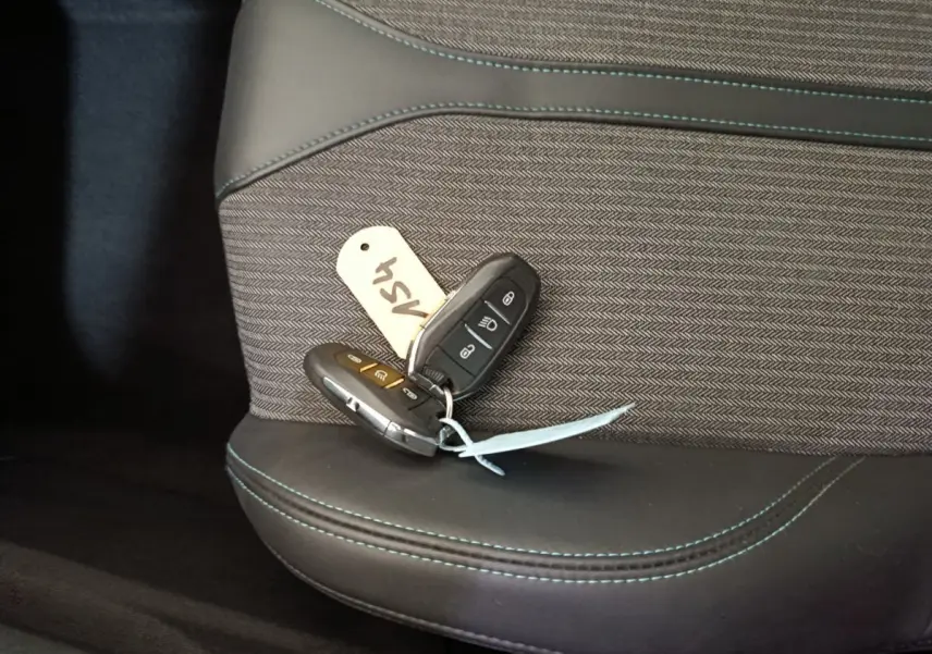 Gros plan sur les clés de la Peugeot 3008 PureTech 130 posées sur un siège tissu et cuir noir avec surpiqûres bleues.