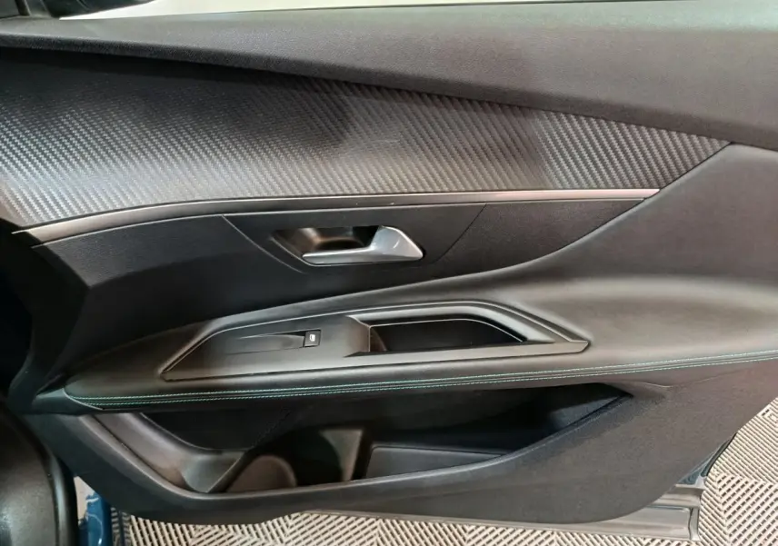 Gros plan sur la porte côté gauche du Peugeot 3008 bleu, avec garniture noire et insert effet carbone.