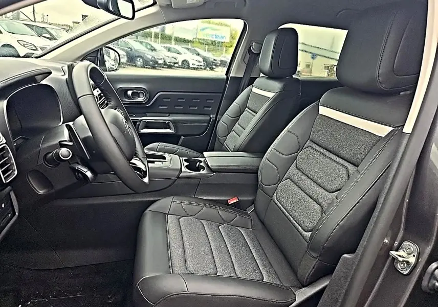 Vue intérieure côté conducteur du Citroën C5 Aircross 2025, sièges noirs cuir et tissu avec accoudoir central.