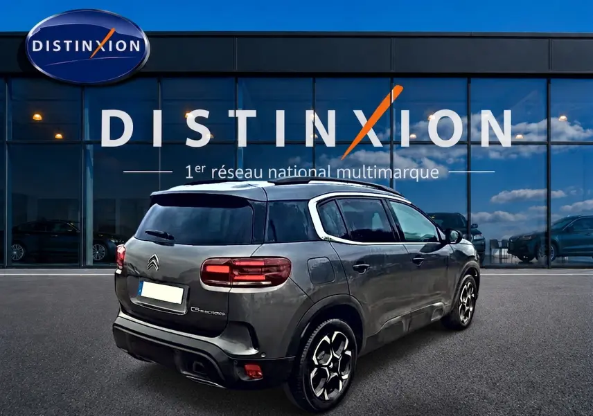 Vue 3/4 arrière droite du Citroën C5 Aircross gris 2025 avec jantes alu et barres de toit visibles.