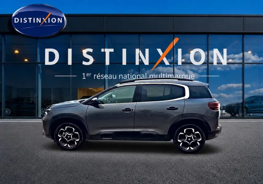 Profil côté gauche du Citroën C5 Aircross gris 2025 avec jantes alu et barres de toit visibles devant un showroom Distinxion.
