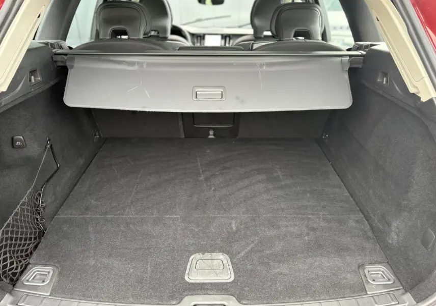 Coffre ouvert du Volvo XC60 rouge Fusion, vue arrière montrant l'espace de chargement avec cache-bagages déployé.