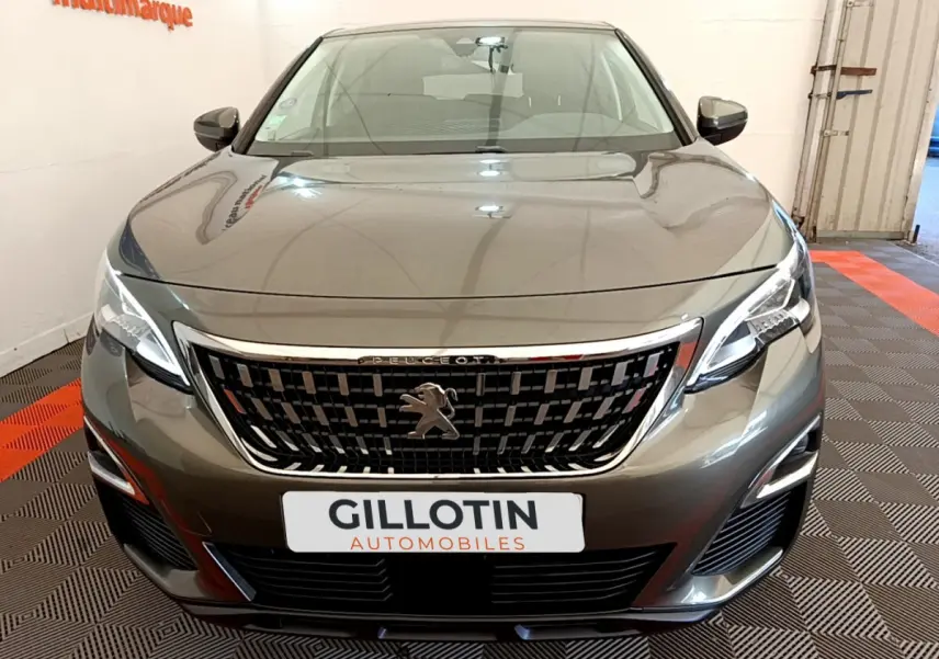 Vue frontale d'un Peugeot 3008 gris foncé avec calandre chromée et phares LED allumés dans un showroom.