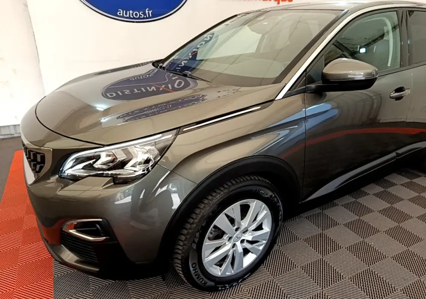Peugeot 3008 gris foncé en 3/4 avant droit, avec phares LED et jantes alliage visibles en intérieur showroom.