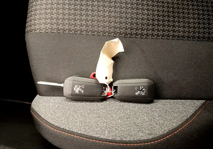 Clé de voiture Peugeot posée sur un siège tissu gris foncé avec surpiqûres rouges, intérieur du 3008 Puretech 2020.