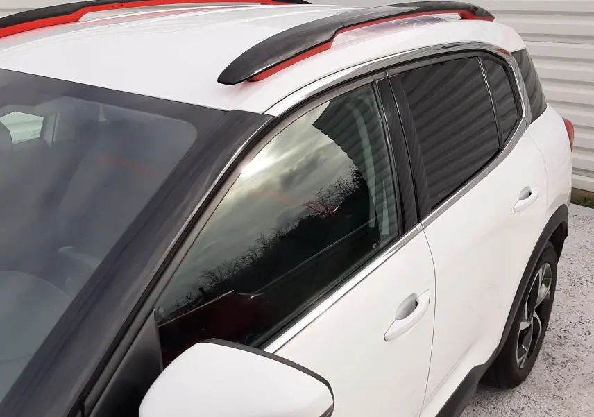 Vue 3/4 avant droit du Citroën C5 Aircross blanc avec barres de toit noires et détails rouges.