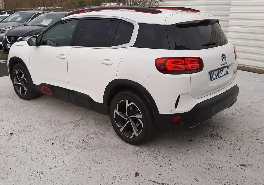 Vue 3/4 arrière droite d'un Citroën C5 Aircross blanc avec toit noir et touches rouges, sur parking extérieur.