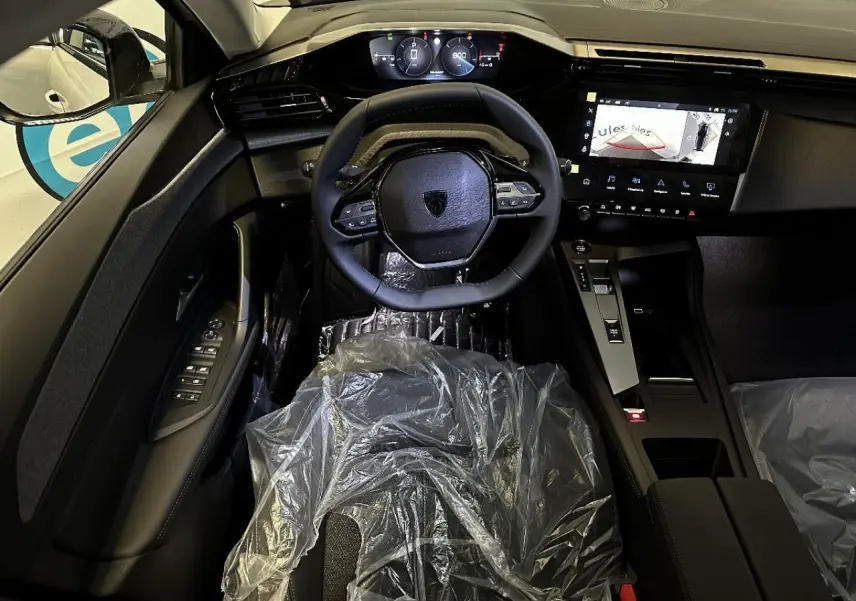 Vue intérieure avant centrée sur le volant compact et le tableau de bord numérique de la Peugeot 308 2024 blanc okenite.