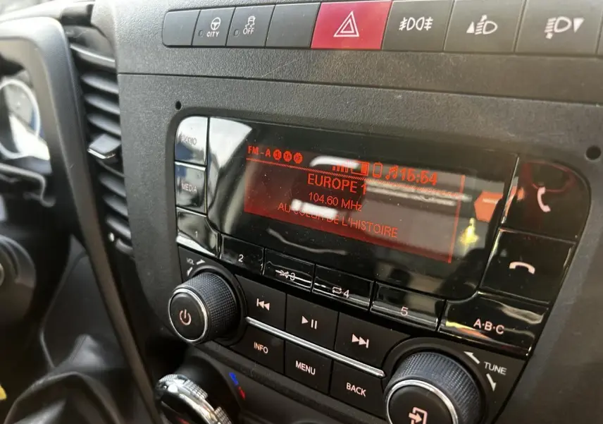 Gros plan sur la radio et les commandes centrales du tableau de bord de l'IVECO Daily blanc, affichant Europe 1 à 104,6 MHz.