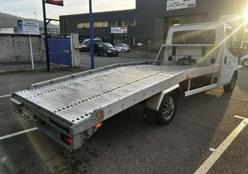 IVECO Daily blanc vu en 3/4 arrière droit, plateau métallique perforé pour transport, stationné en extérieur au soleil.