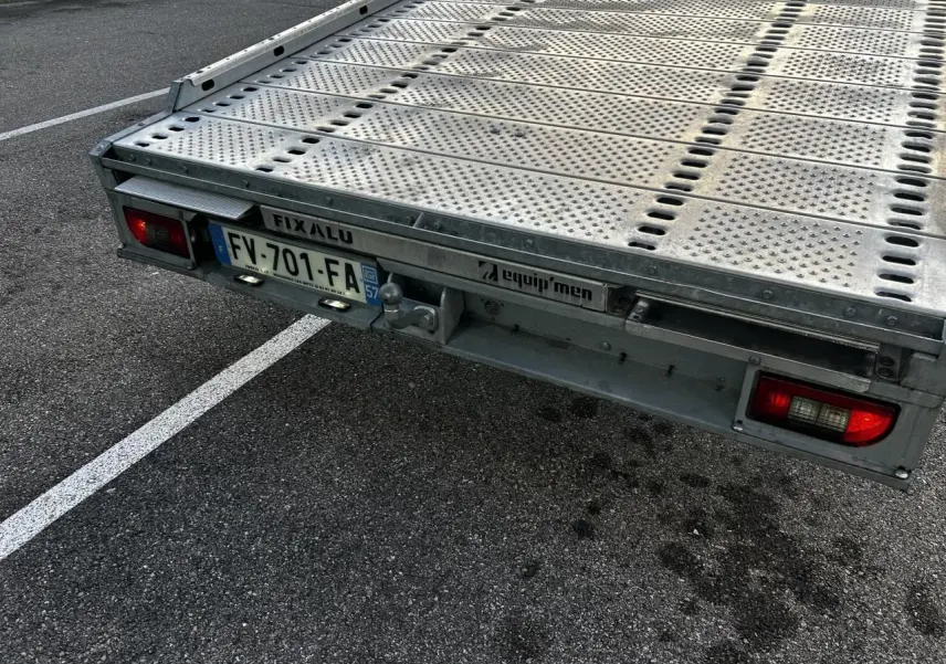 Plateau arrière en métal d'un Iveco Daily blanc, vu en gros plan depuis l'arrière droit avec plaque d'immatriculation française.