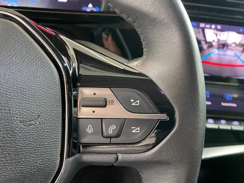 Vue rapprochée des commandes au volant côté droit d'une Peugeot 308 gris Artense avec écran de caméra de recul en arrière-plan.