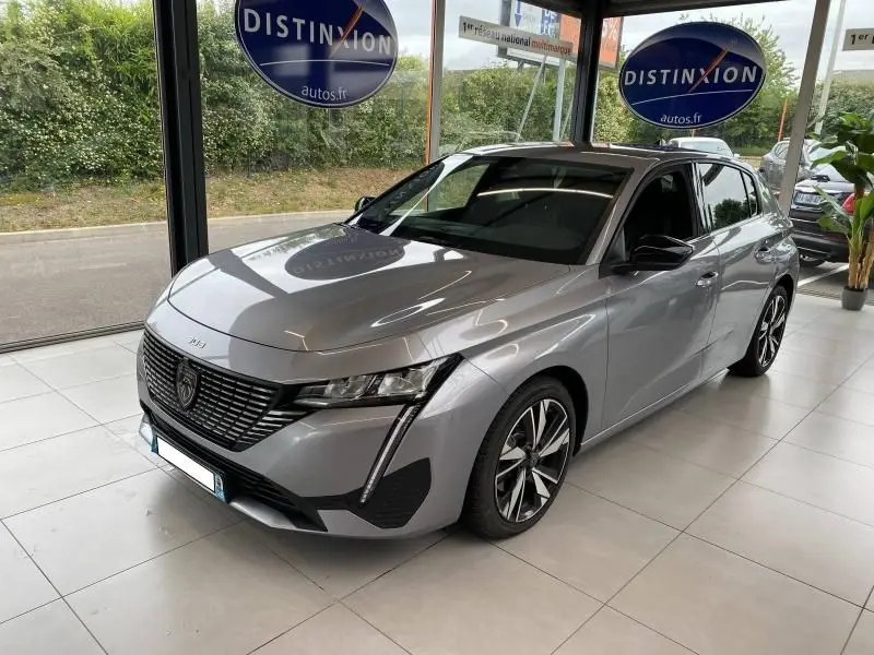 Peugeot 308 gris Artense vue 3/4 avant droit en showroom avec calandre noire et jantes alliage distinctives.