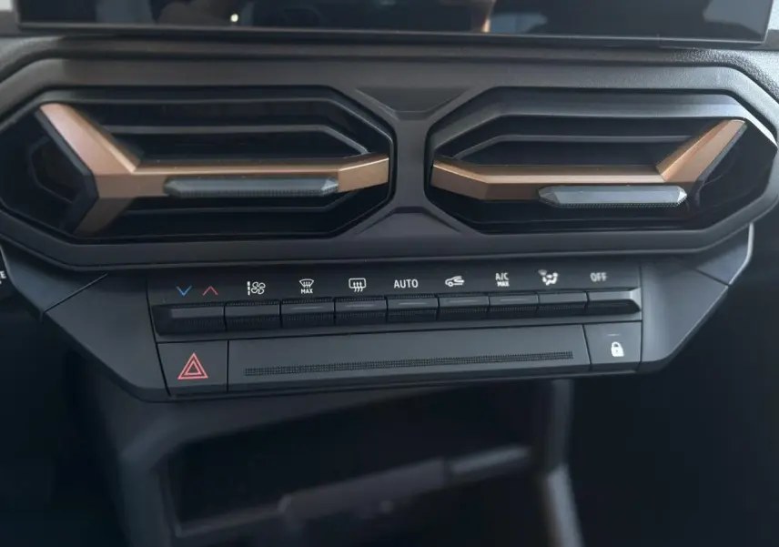 Détail du tableau de bord du Dacia Duster 2026, avec aérateurs brun cuivré et commandes de climatisation noires.
