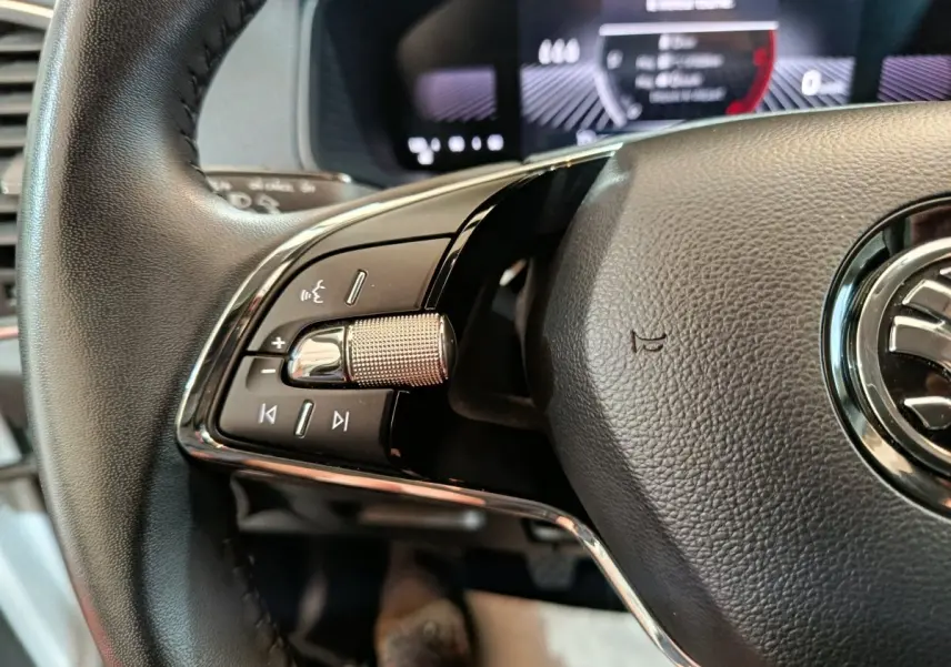 Gros plan sur la partie gauche du volant cuir noir du Skoda Karoq 2024, avec commandes intégrées et logo visible.