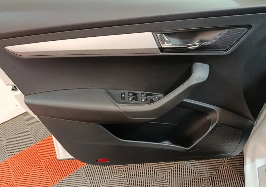 Porte côté gauche ouverte d'un Skoda Karoq blanc 2024, avec commandes de vitres et garniture noire.