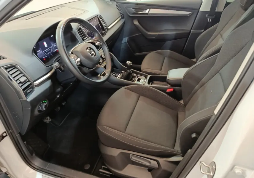 Intérieur avant droit d'une Skoda Karoq blanc 2024, volant cuir, sièges tissu noirs et tableau de bord digital.