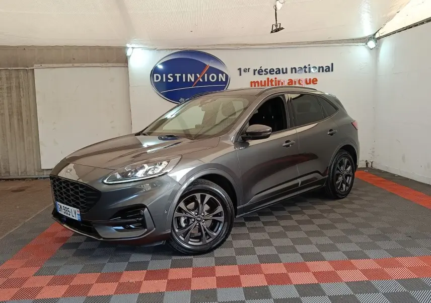 Ford Kuga gris foncé en 3/4 avant droit, avec jantes noires et calandre imposante dans un showroom.