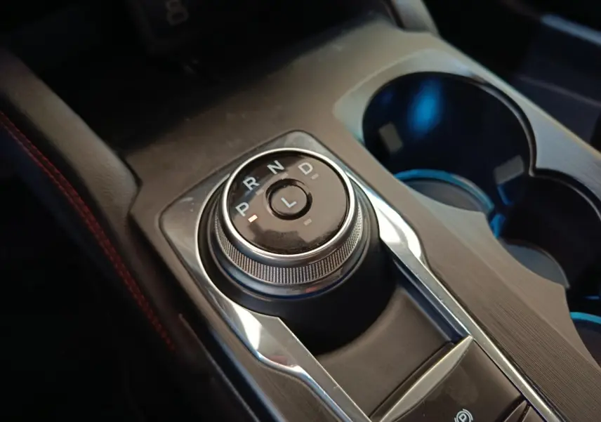 Gros plan sur la molette de boîte automatique noire et argentée du Ford Kuga gris foncé, avec porte-gobelets à côté.