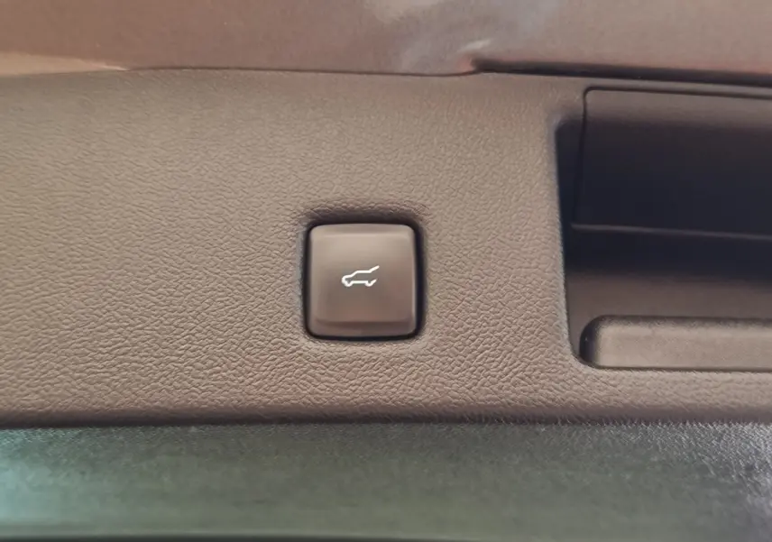 Bouton d'ouverture électrique du coffre sur le panneau intérieur d'un Ford Kuga gris foncé, vue rapprochée.