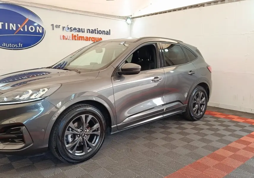 Vue 3/4 avant droit d’un Ford Kuga gris foncé 2023 avec jantes alliage et toit noir dans un showroom.