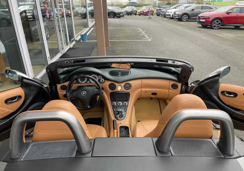 Vue intérieure de la Maserati Spyder 2002 avec tableau de bord et sièges en cuir beige, portes ouvertes et volant noir.