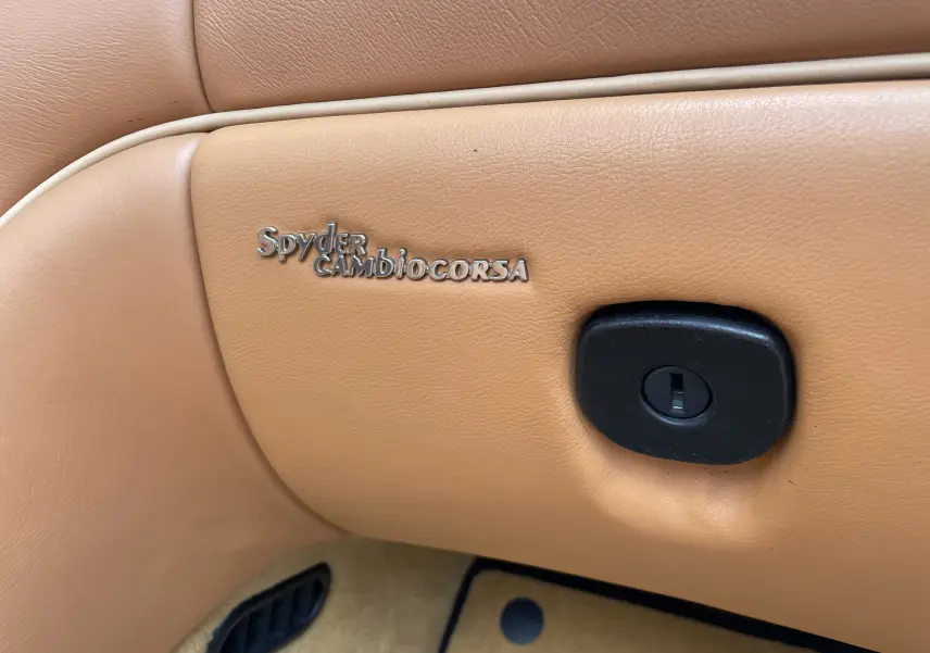 Gros plan sur le badge Spyder Cambiocorsa incrusté dans le cuir beige de l’habitacle d’une Maserati Spyder 2002.