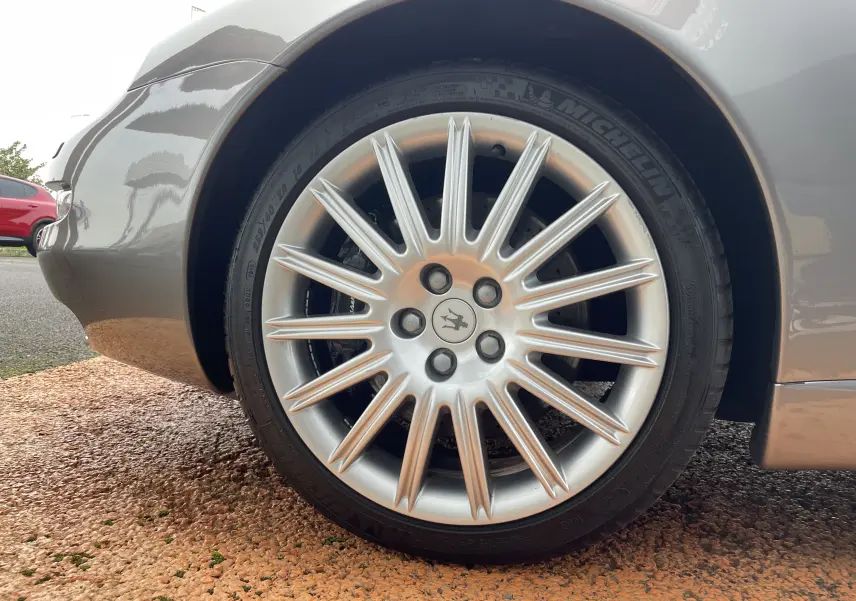 Gros plan sur la roue avant gauche gris nuvolari d'une Maserati Spyder 2002 avec jante multibranches et logo trident central.