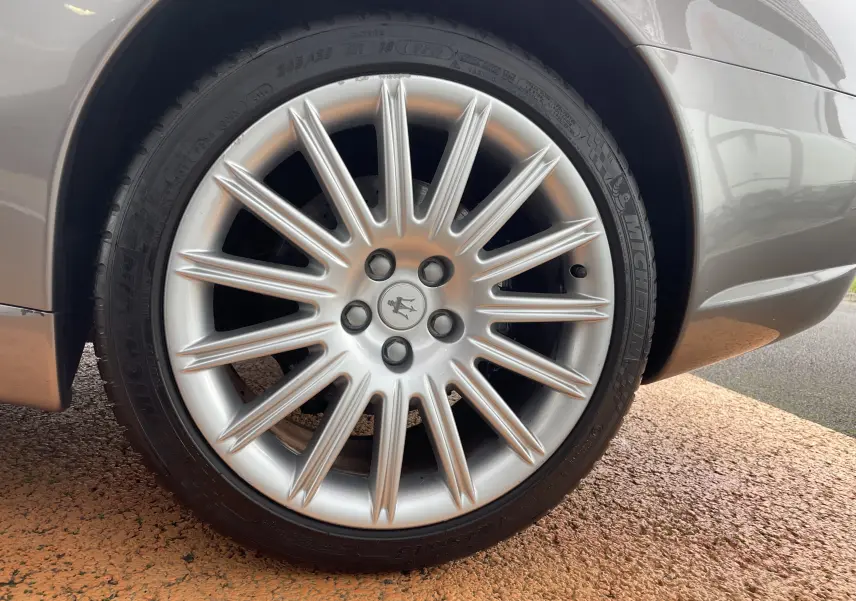 Gros plan sur la roue avant droite grise Nuvolari d'une Maserati Spyder 2002 avec jante argentée au logo trident.